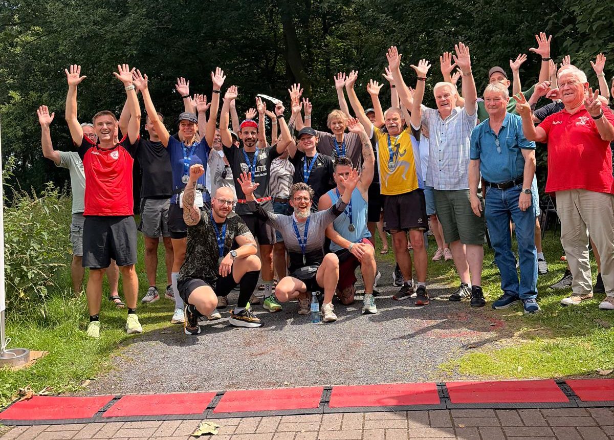 Läuferinnen, Läufer und Helfer jubeln mit erhobenen Armen hinter den roten Zeitmessmatten im Sportpark Eickel